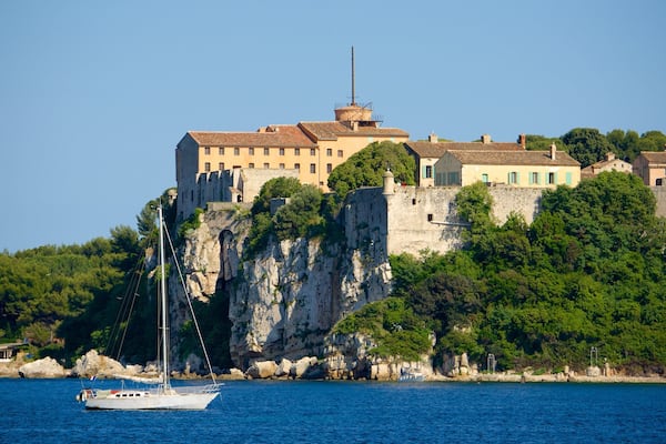 Eine Küstenstadt mit einem markanten Schloss auf einem Felsen, umgeben von üppiger Vegetation und blauem Meer.