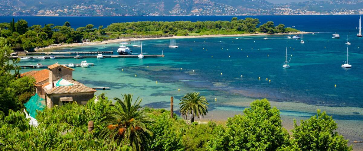 A coastal town with clear turquoise waters, boats, and a backdrop of mountains.