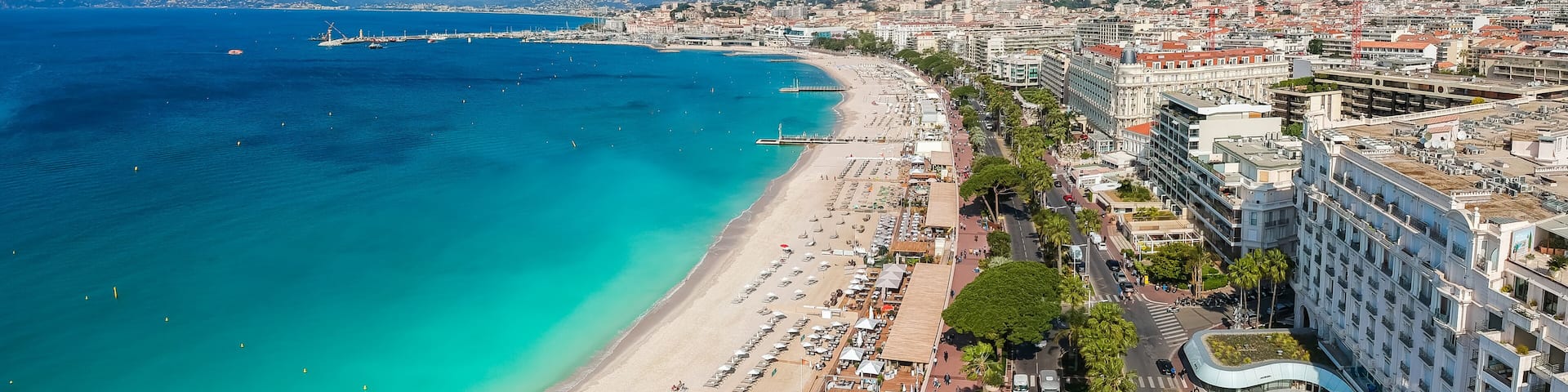 A coastal cityscape with a beach, urban buildings, and a distant mountain range.