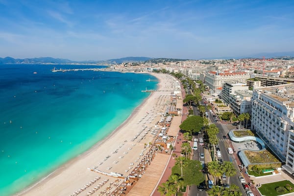 Un paysage urbain côtier avec une plage, des bâtiments de la ville et une chaîne de montagnes en arrière-plan.