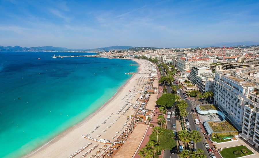 A coastal cityscape with a beach, urban buildings, and a distant mountain range.