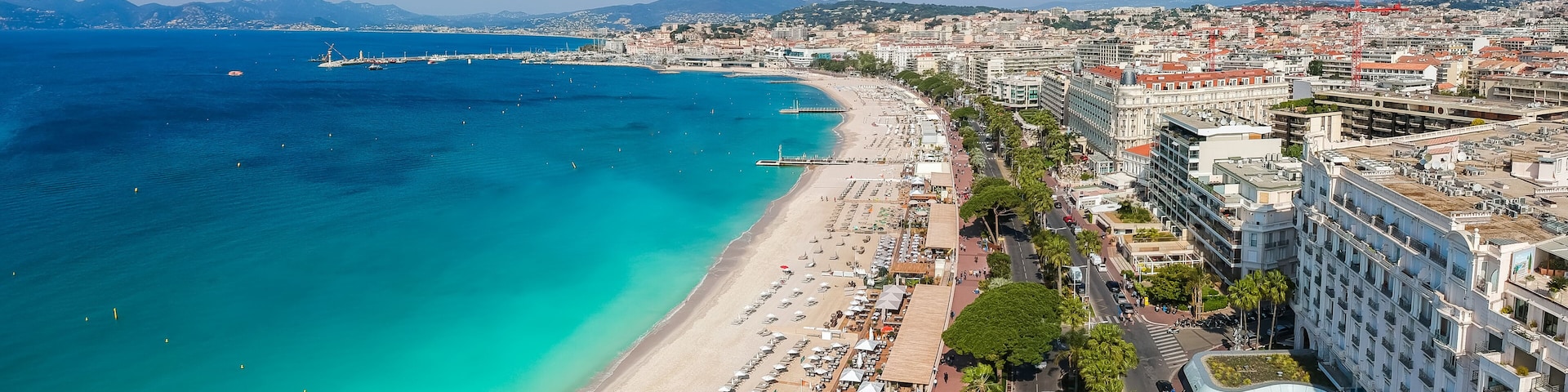 A coastal cityscape with a beach, urban buildings, and a distant mountain range.