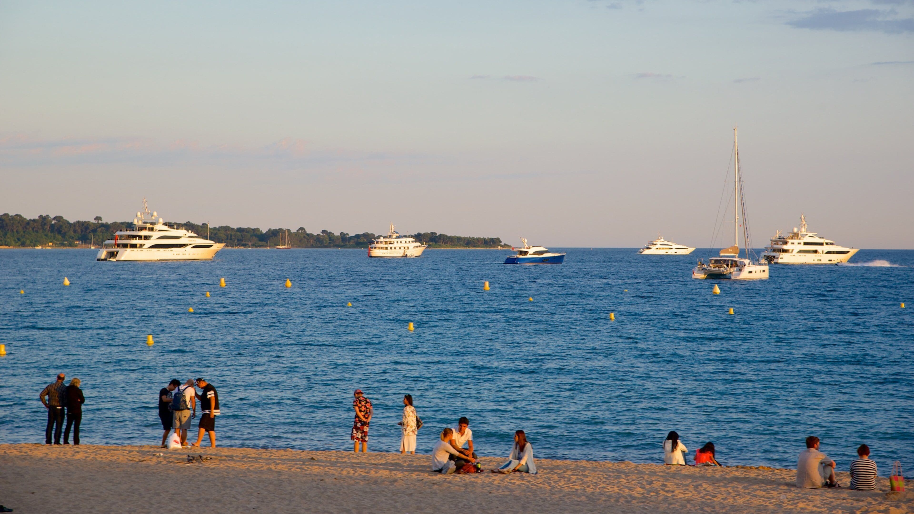 A beach with people relaxing and several yachts in the water.