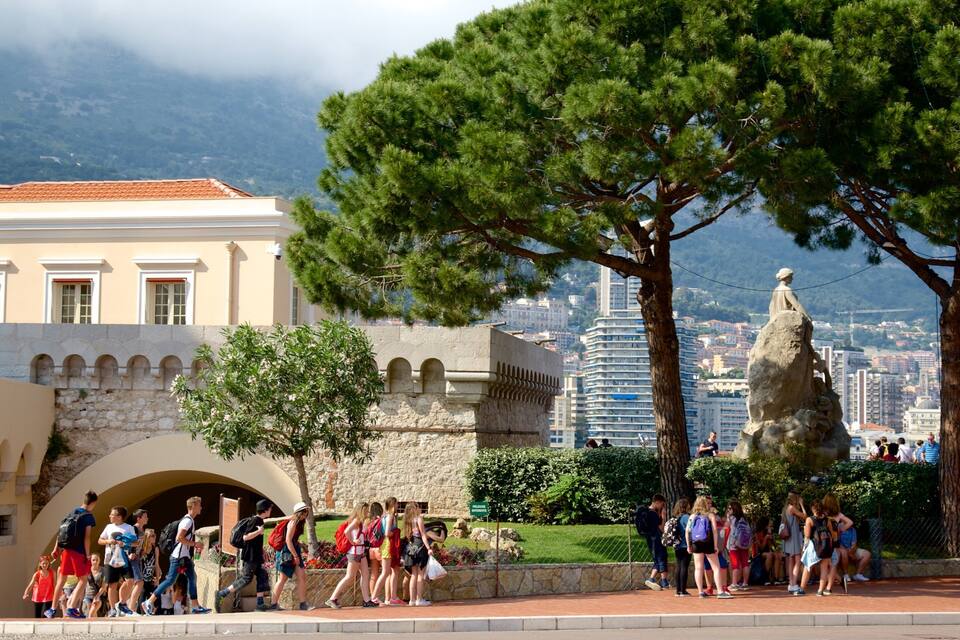 Un grupo de personas reunidas alrededor de una estatua en un parque, con un paisaje urbano de fondo.