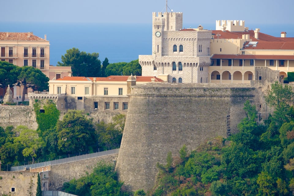 A historic castle with a stone wall, a clock tower, and a view of the sea.