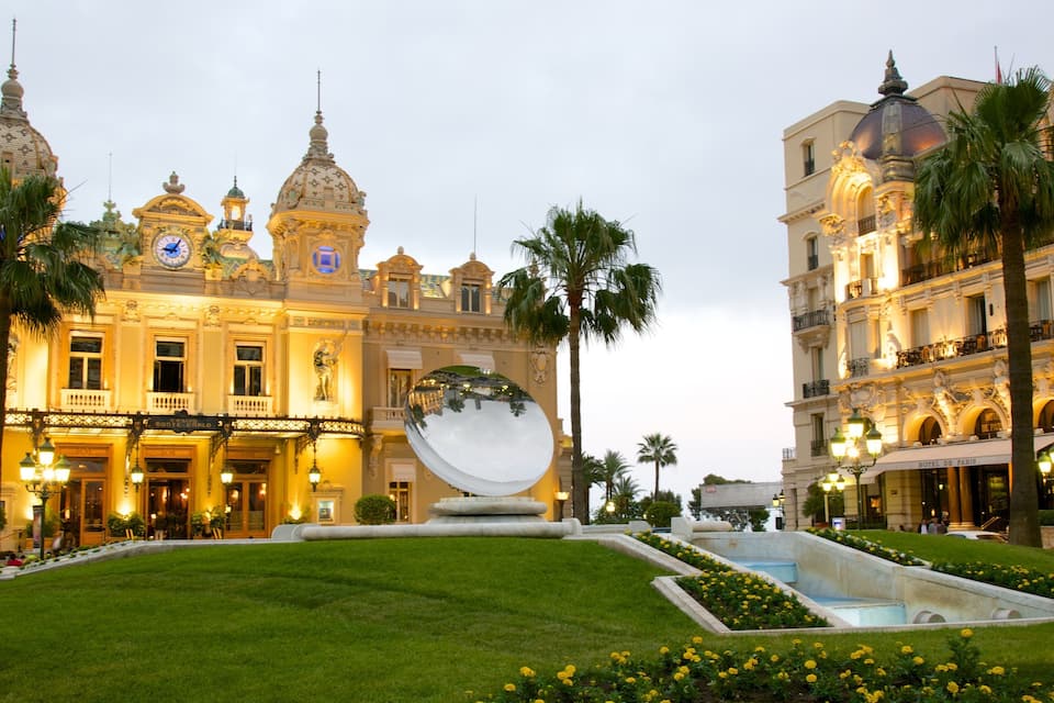 A grand building with ornate architecture, a large reflective sphere, and well-maintained gardens.