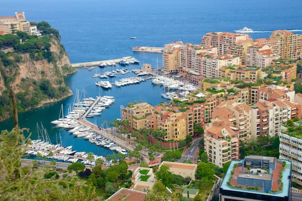 A coastal cityscape with a marina filled with boats, residential buildings, and a cliff overlooking the sea.