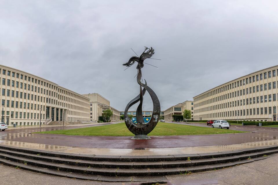 A sculpture in a plaza with two large buildings on either side.