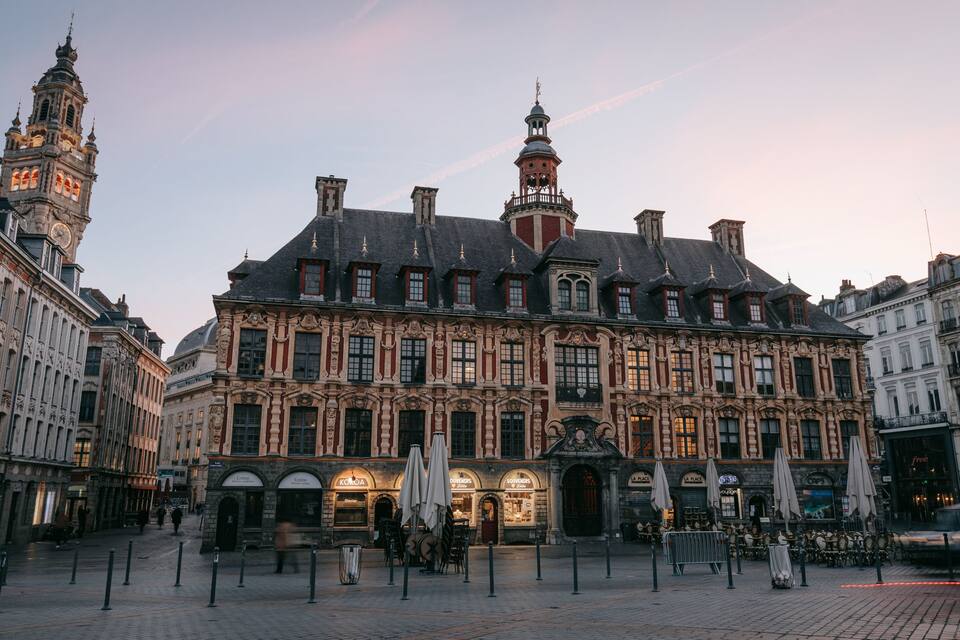 A historic building with ornate architecture, a clock tower, and a plaza with outdoor seating.