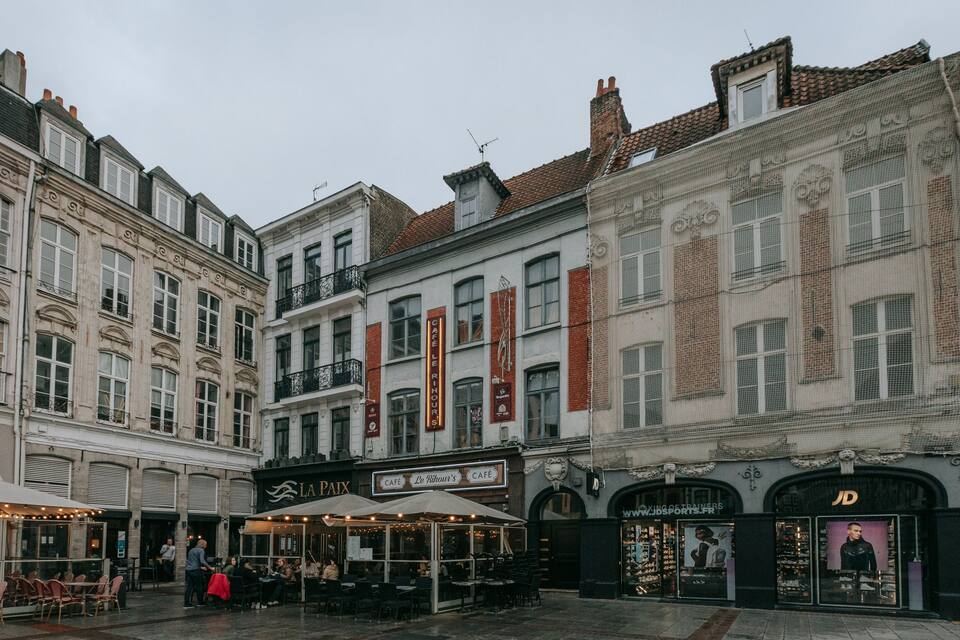 A historic European street with cafes and shops, including 'La Paix' and 'Le Rihour's'.