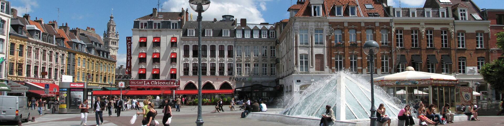 A bustling square with historic buildings, a fountain, and people walking around.