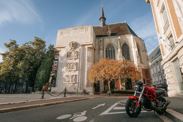 Ein historisches Gebäude mit Inschriften, einer Statue und einem Baum mit Herbstlaub.