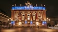 A grand illuminated building with statues and ornate architecture at night.