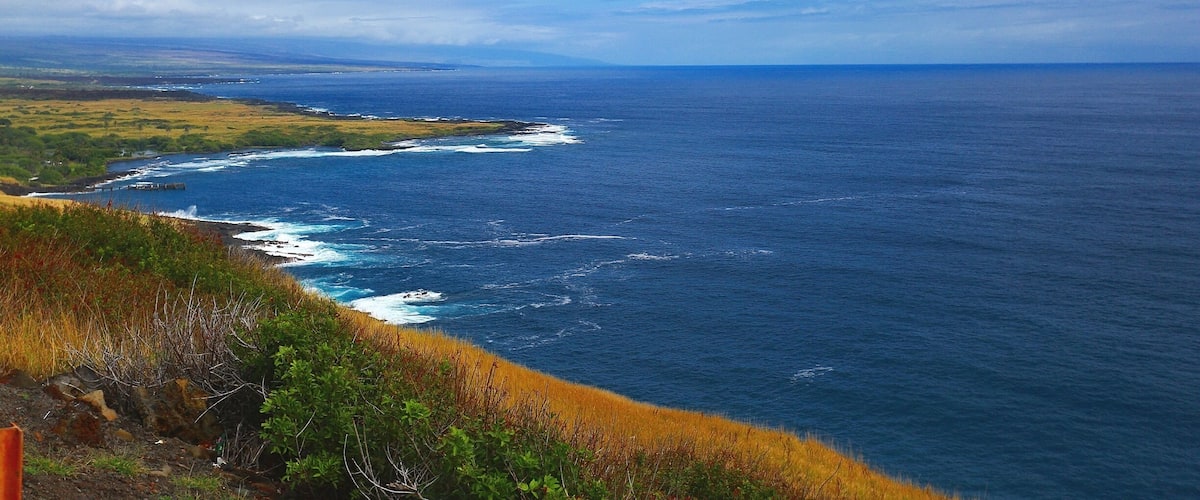 The beautiful Pacific Ocean just around the bend at South Point At Big Island, Hawaii. Blue skies, bluer waters and green green grass! Beautiful!
