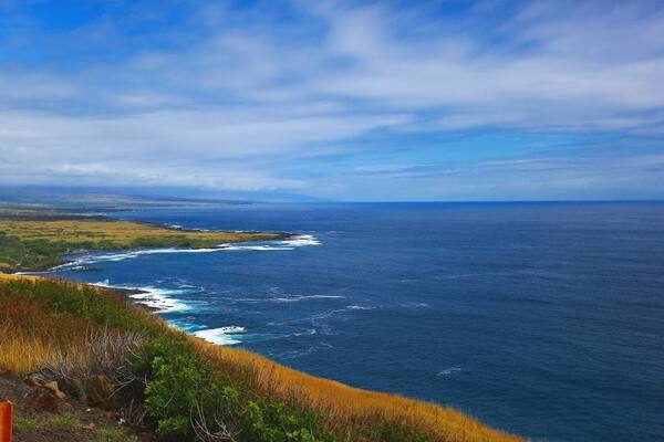 The beautiful Pacific Ocean just around the bend at South Point At Big Island, Hawaii. Blue skies, bluer waters and green green grass! Beautiful!