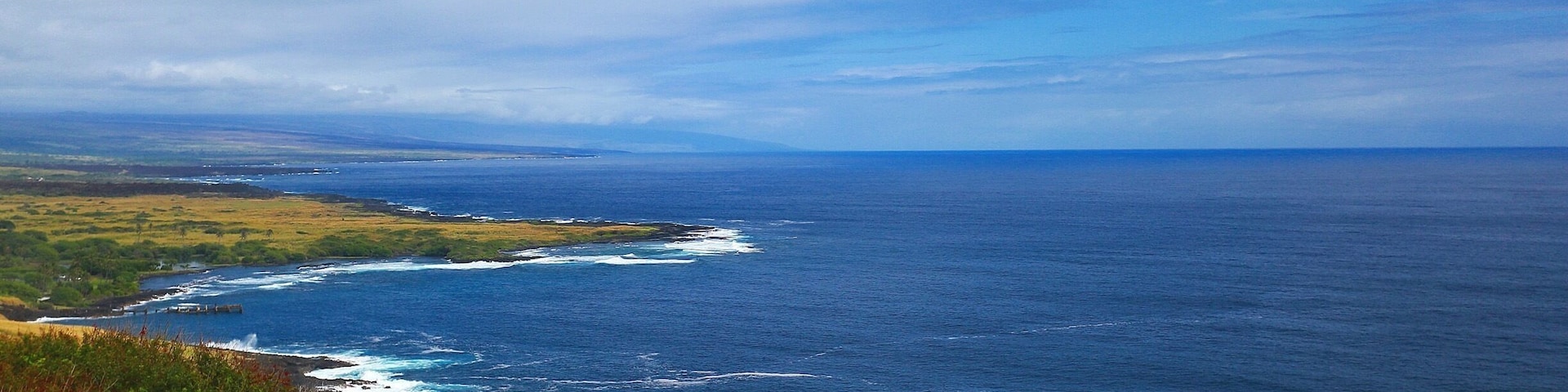 The beautiful Pacific Ocean just around the bend at South Point At Big Island, Hawaii. Blue skies, bluer waters and green green grass! Beautiful!