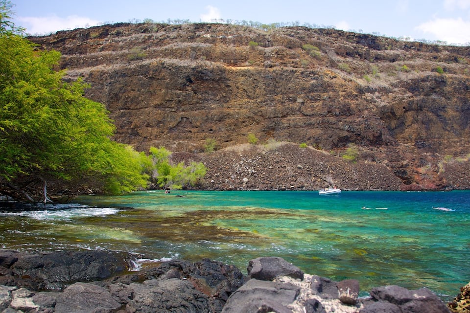 A coastal landscape with clear turquoise waters, rocky terrain, and green vegetation.