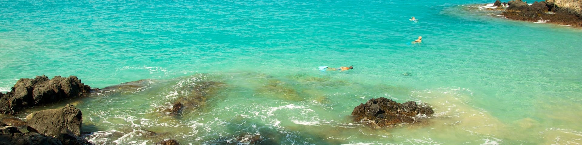 A turquoise sea with clear waters, rocky shoreline, and a distant landmass.