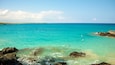 A turquoise sea with clear waters, rocky shoreline, and a distant landmass.