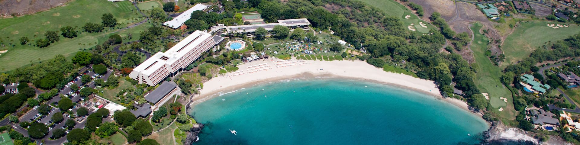 An aerial view of a coastal area with a beach, golf course, and residential buildings.
