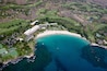 An aerial view of a coastal area with a beach, golf course, and residential buildings.