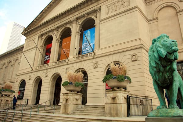 Edifício do Instituto de Arte de Chicago com arquitetura clássica, uma estátua de leão e banners anunciando eventos.