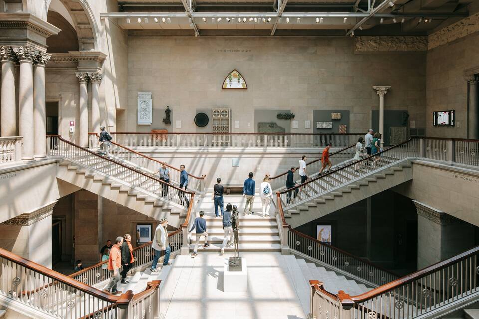 Una majestuosa escalera en un edificio histórico con arquitectura clásica, incluyendo columnas y barandillas ornamentadas.