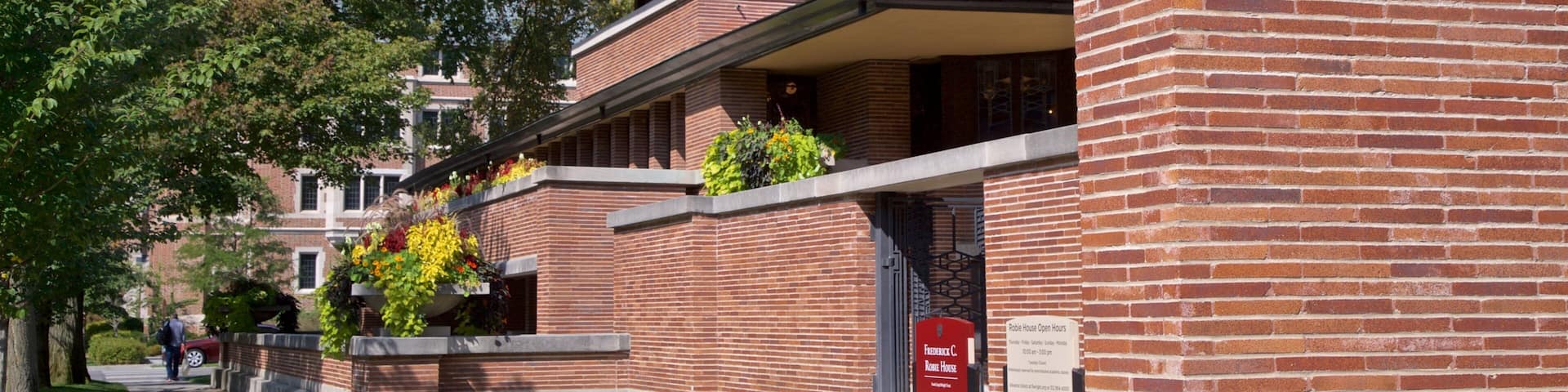 Un edificio de ladrillo con un letrero rojo, árboles verdes y un cielo despejado.
