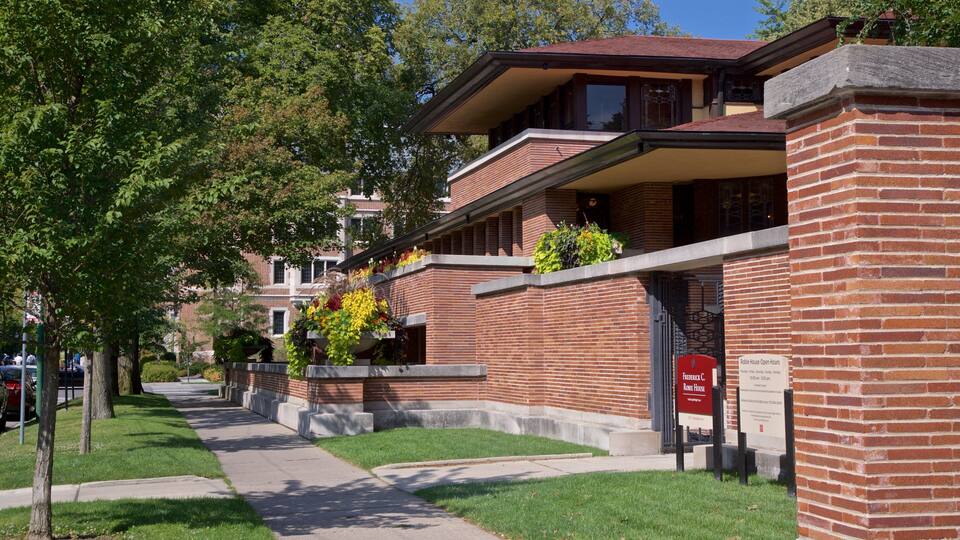 A brick building with a red roof, a mailbox, and a sign indicating the Robie House Open Hours.
