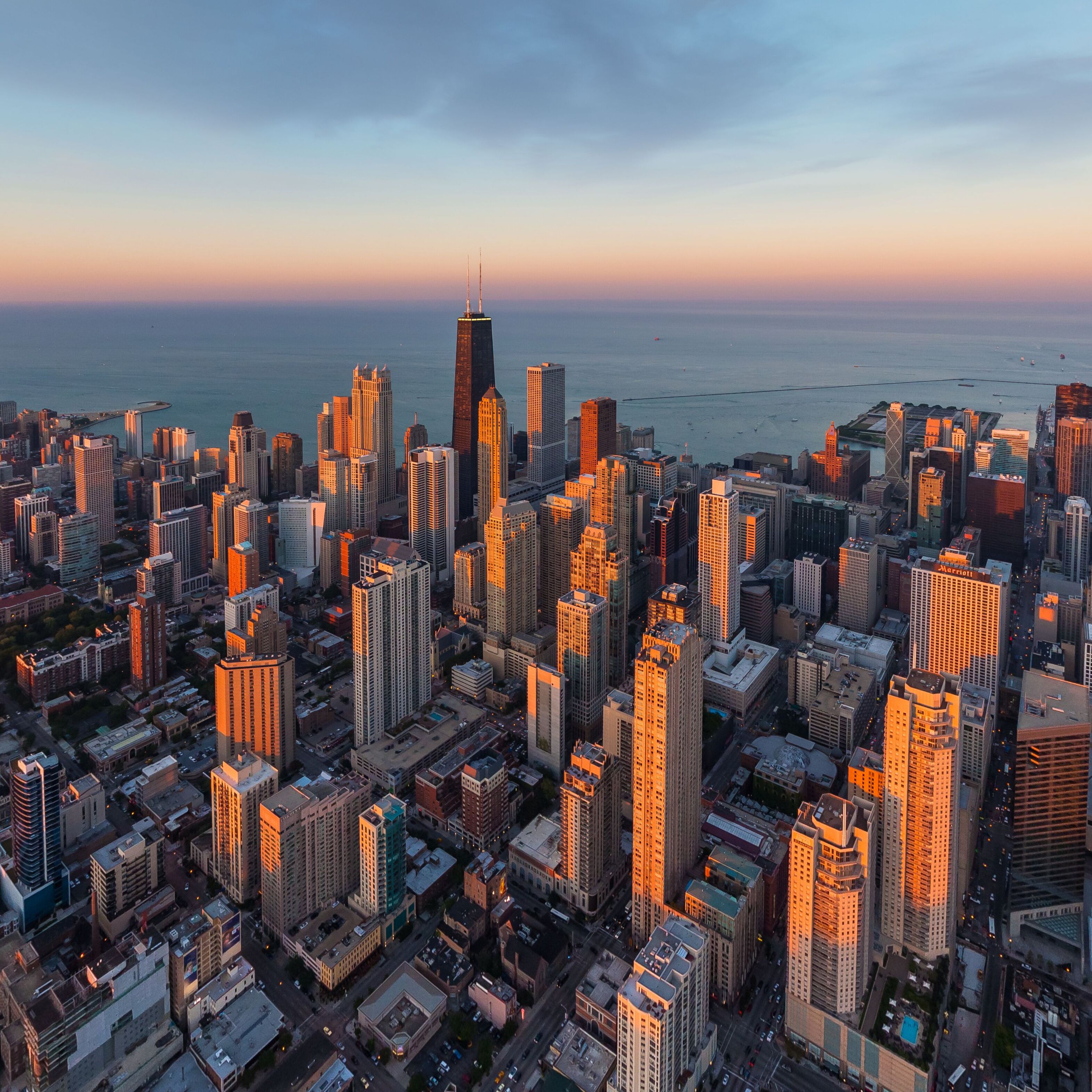 Aerial view of skyscrapers basking in the golden light of the setting sun, with the iconic John Hancock Center piercing the skyline, Chicago, Illinois, United States.