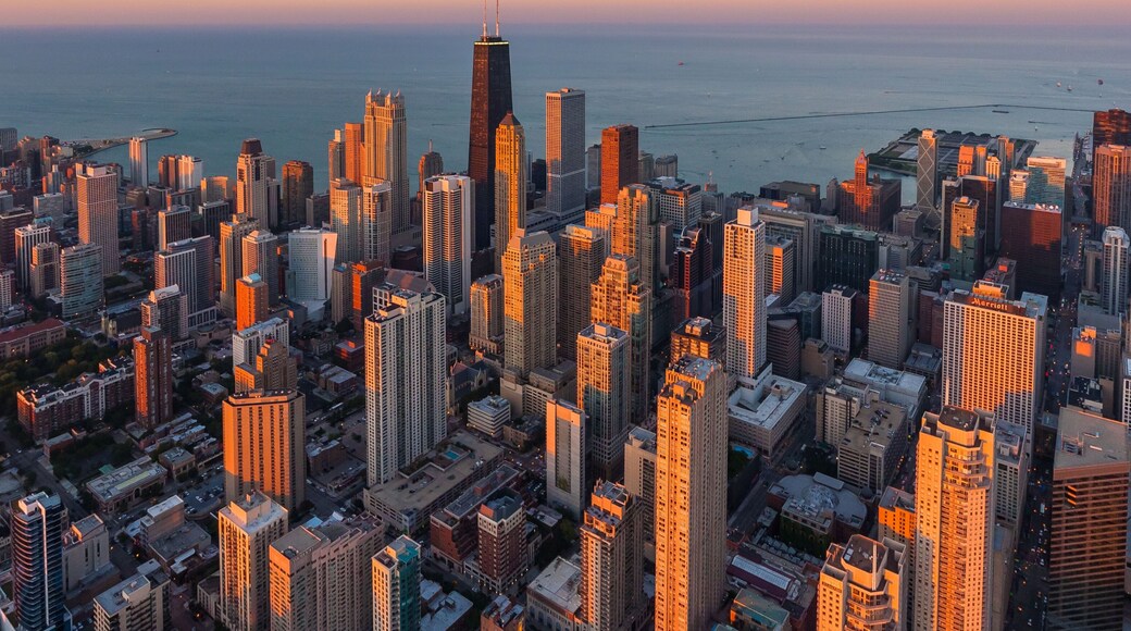 Aerial view of skyscrapers basking in the golden light of the setting sun, with the iconic John Hancock Center piercing the skyline, Chicago, Illinois, United States.