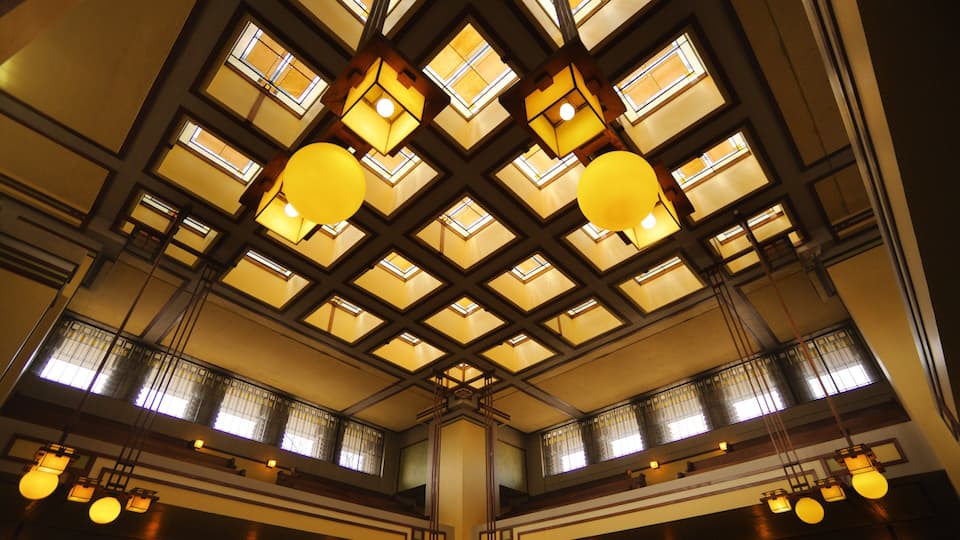 A building interior with a high ceiling, geometric wooden beams, and multiple hanging spherical light fixtures.