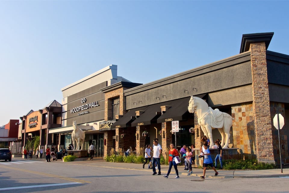 Una calle con un edificio que dice 'Woodfield Mall' y una estatua de un caballo.