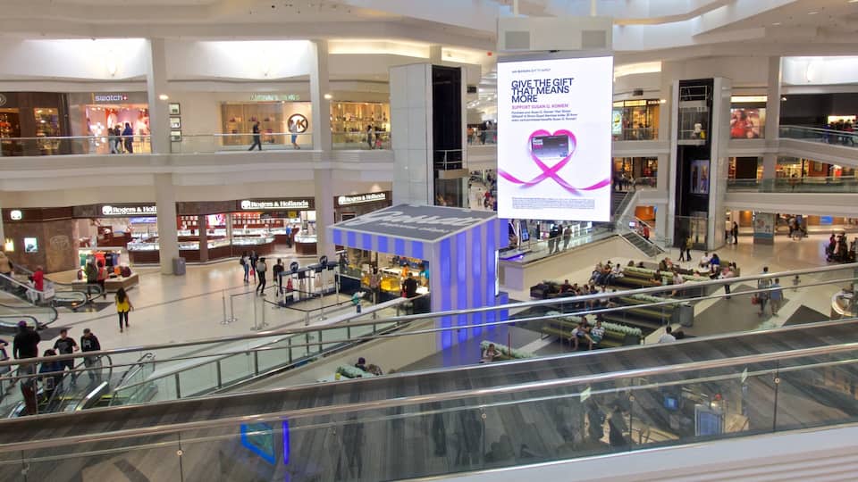 A multi-level shopping mall with escalators, various retail stores, and a large digital advertisement.