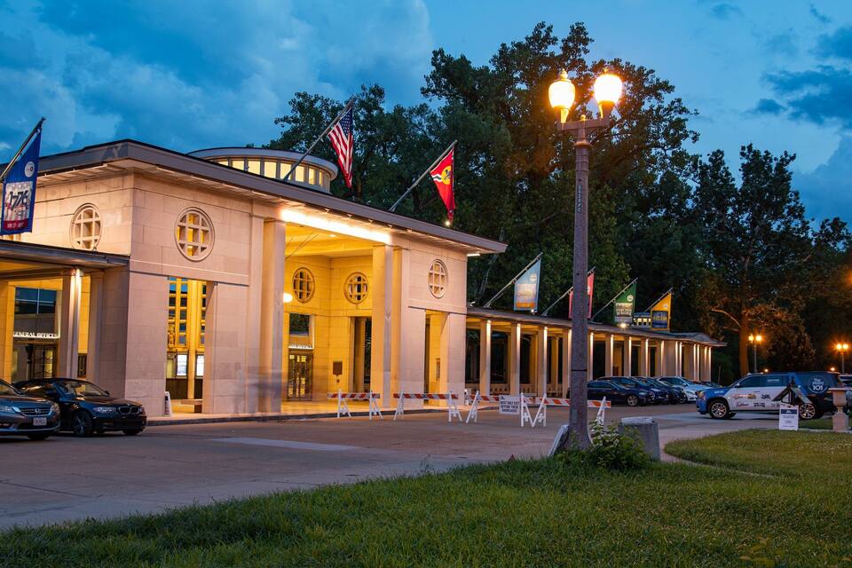 A well-lit building with multiple flags, including the American flag, and a parking area with cars.