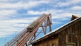 A wooden roller coaster with a steep incline and a wooden building in the foreground.