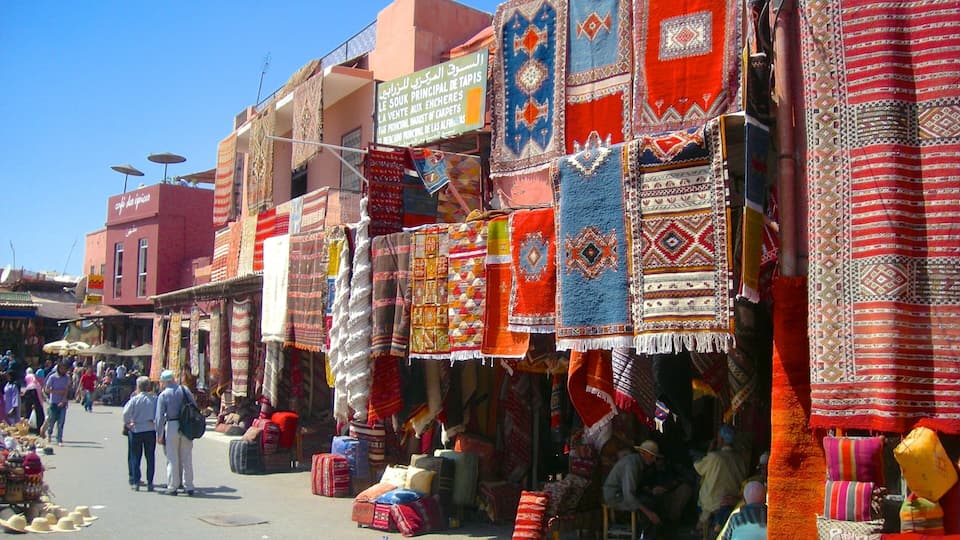 A bustling market street with colorful textiles and traditional rugs displayed for sale.