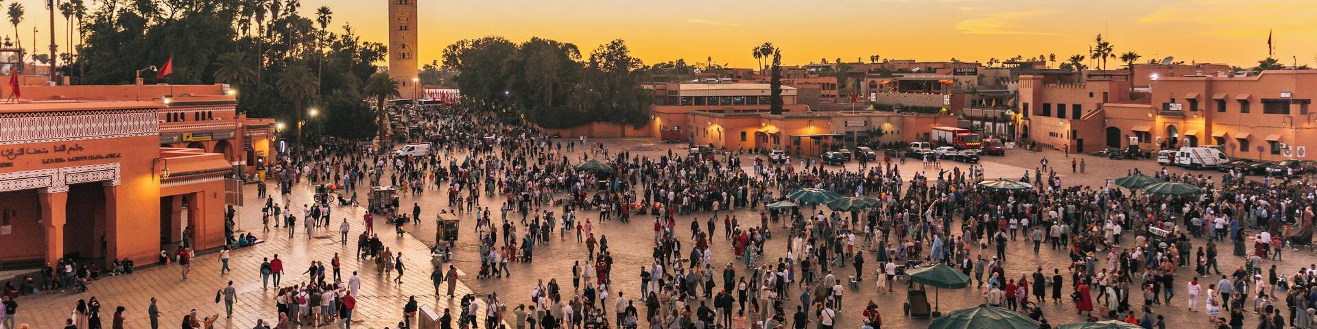 A bustling square with a prominent tower, surrounded by traditional buildings and palm trees.