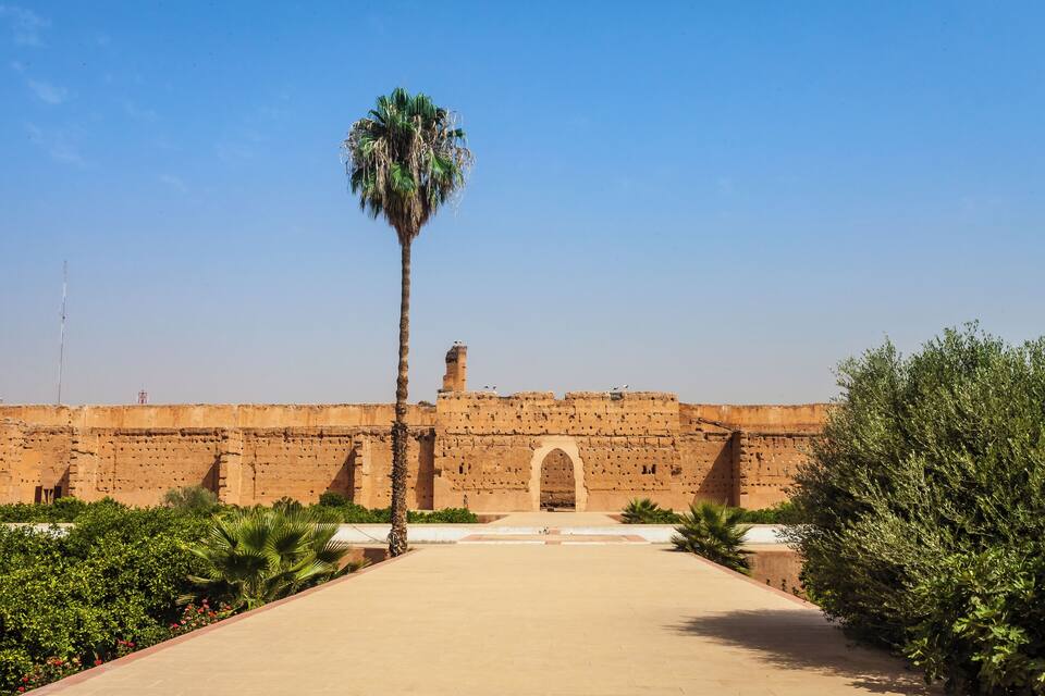 Una fortaleza histórica con un arco central, palmeras y un cielo azul despejado.
