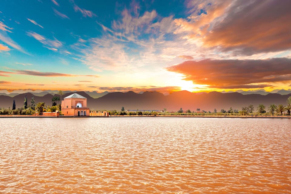 A sunset over a body of water with a small building and mountains in the background.