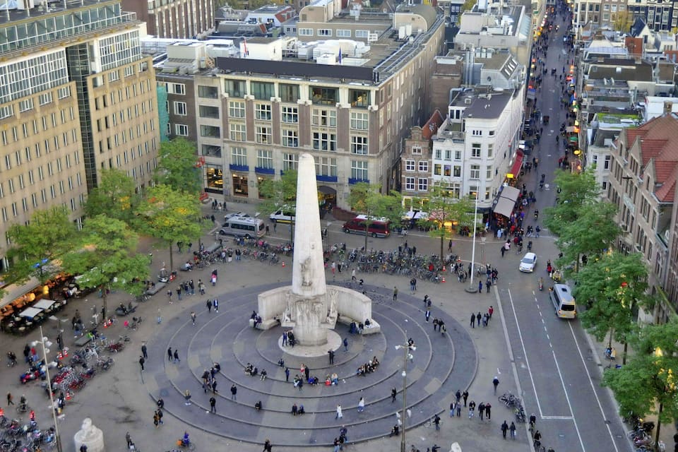 A busy urban square with a central monument, surrounded by historic buildings and a bustling street.