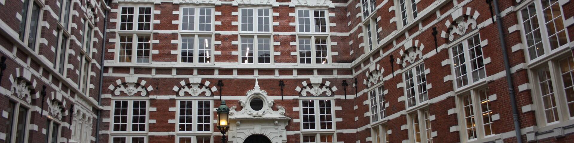 traditional inner courtyard surrounded by tall and old red brick walls. old building, vintage Dutch style. fascinating amsterdam building used as a university