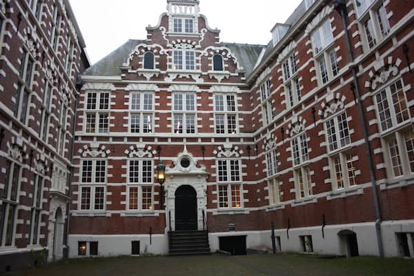 traditional inner courtyard surrounded by tall and old red brick walls. old building, vintage Dutch style. fascinating amsterdam building used as a university