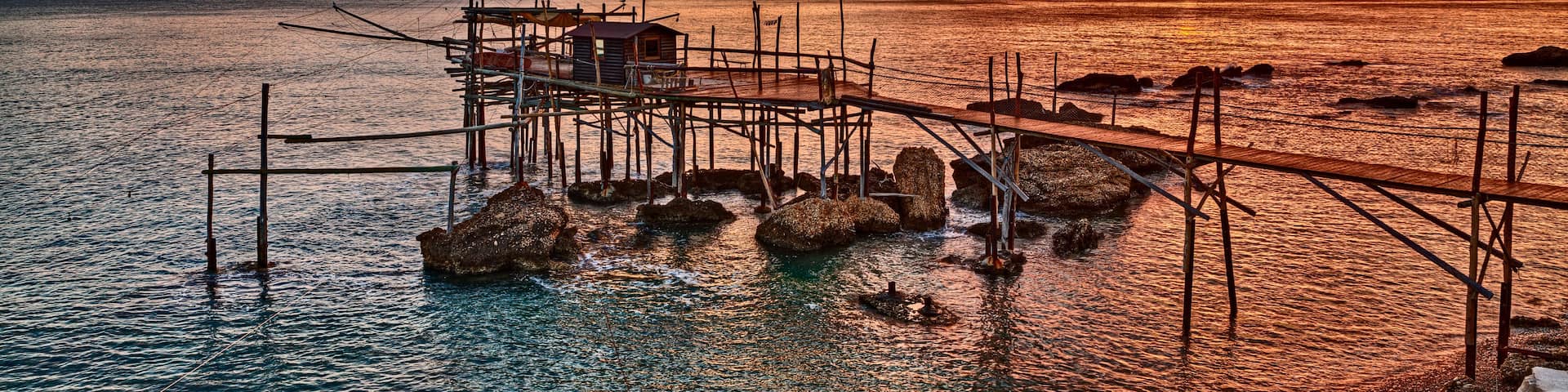 A sunset over a coastal area with a pier extending into the water, surrounded by rocks.