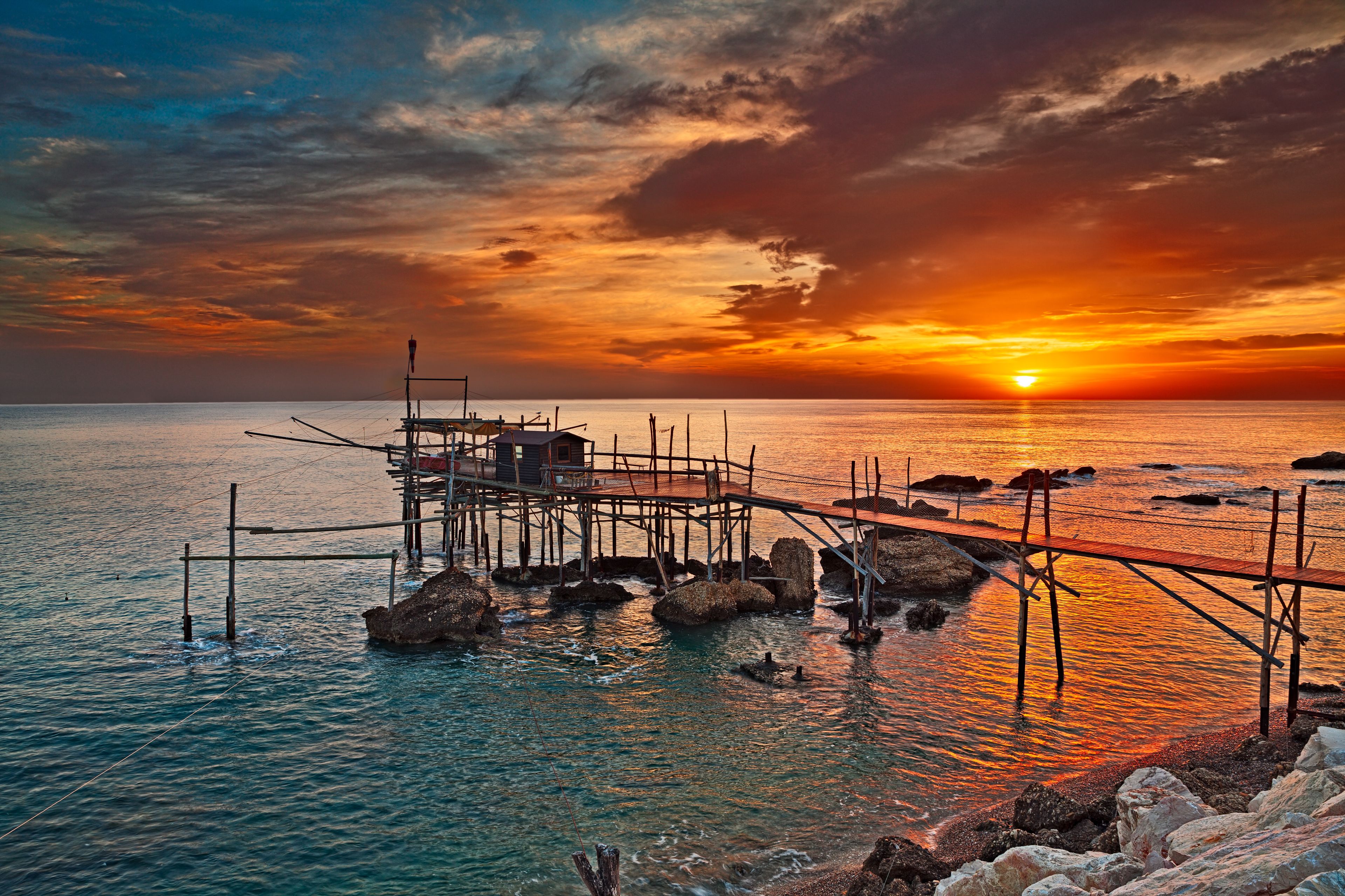 A sunset over a calm sea with a wooden pier extending into the water.