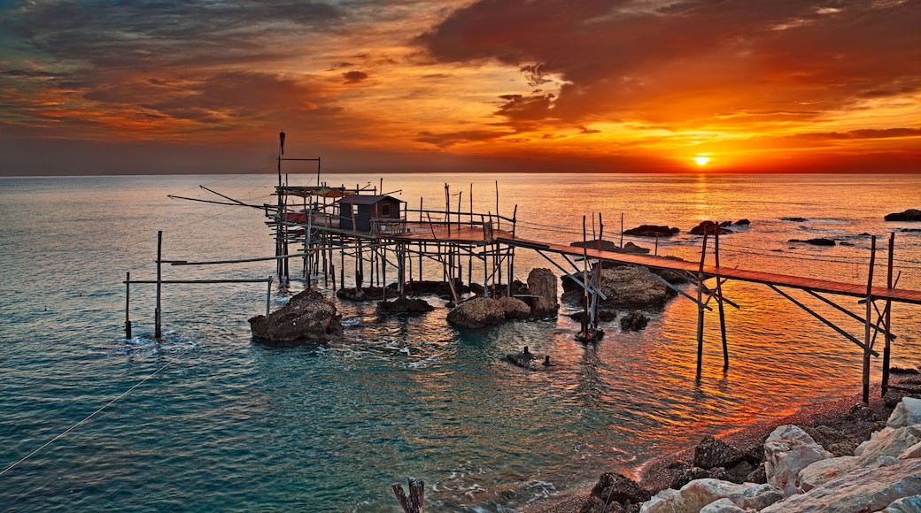 A sunset over a calm sea with a wooden pier extending into the water.