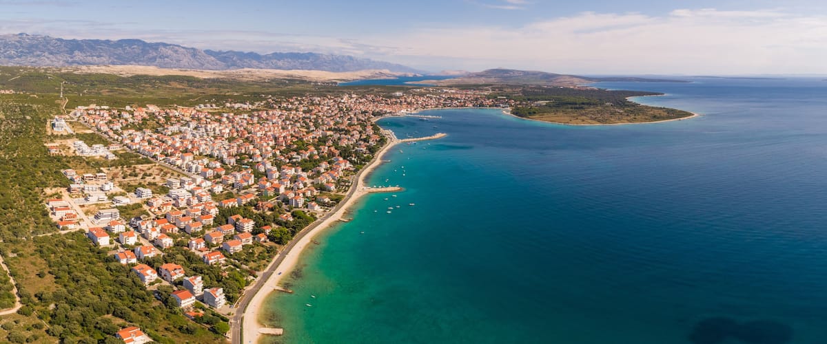 A coastal town with a long beachfront, clear turquoise waters, and a mountainous backdrop.