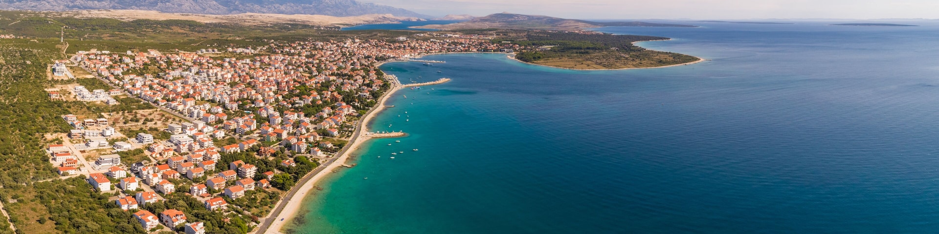 A coastal town with a long beachfront, clear turquoise waters, and a mountainous backdrop.