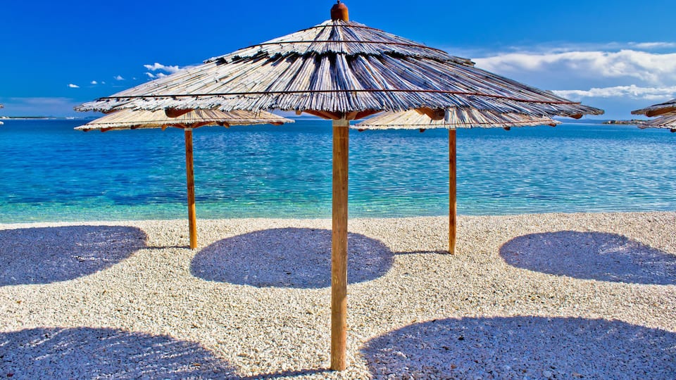 A beach with thatched umbrellas and pebbled sand.