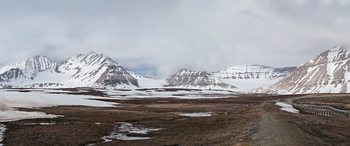 A rugged mountain landscape with snow-covered peaks and a railway track.